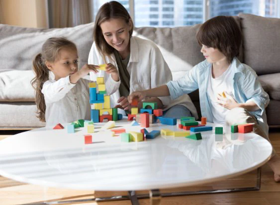 Woman playing with two kids at a table in a living space.