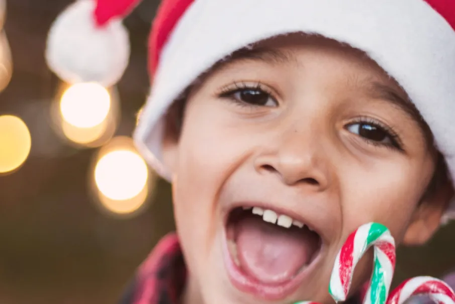 child wearing Santa hat holding candy canes and smiling.