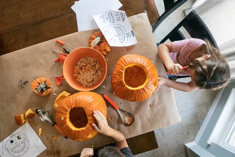 Kids carving pumpkins with tools and drawings on table