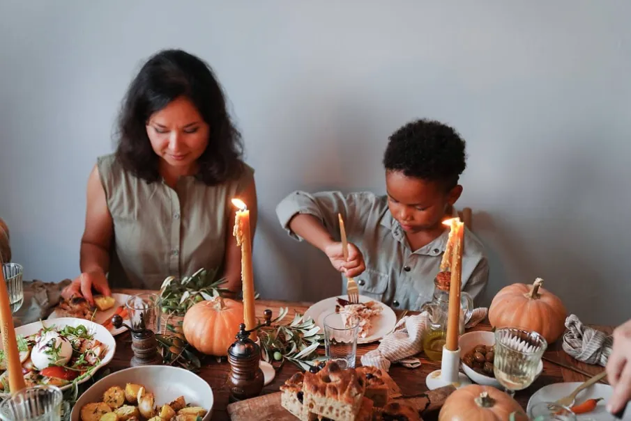 Family enjoying a candlelit Thanksgiving dinner with pumpkin decorations.